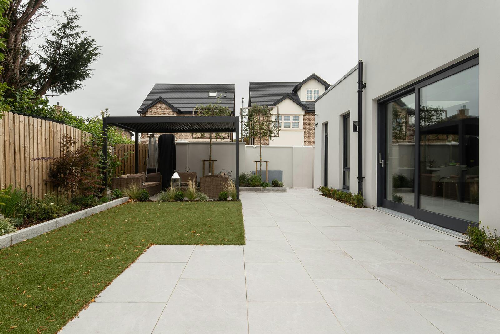 Contemporary backyard featuring a black pergola, lush greenery, and large tiled patio showcasing modern outdoor living trends