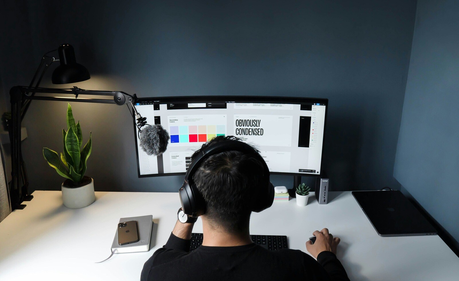 Designer wearing headphones working on a dual monitor setup, reviewing typography and color palettes on the screen