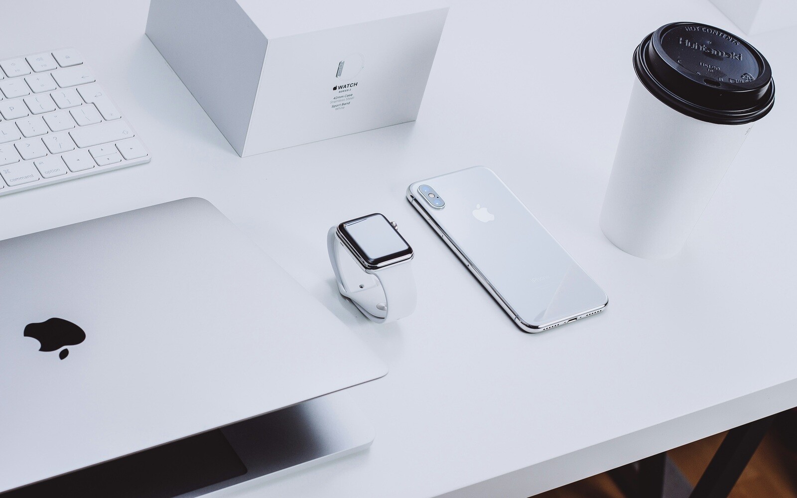 Minimalist desk setup with Apple devices, including a MacBook, iPhone, Apple Watch, and a coffee cup