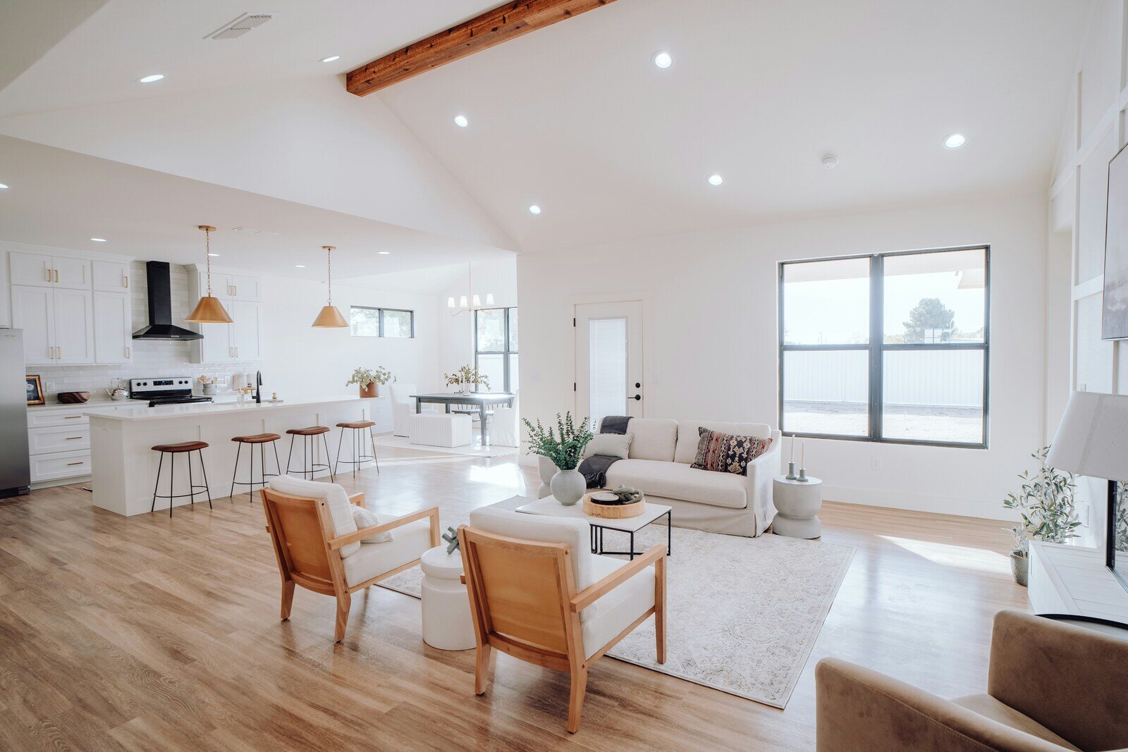 Modern open concept kitchen and living room featuring white cabinetry, large island, wooden stools, and neutral decor trends