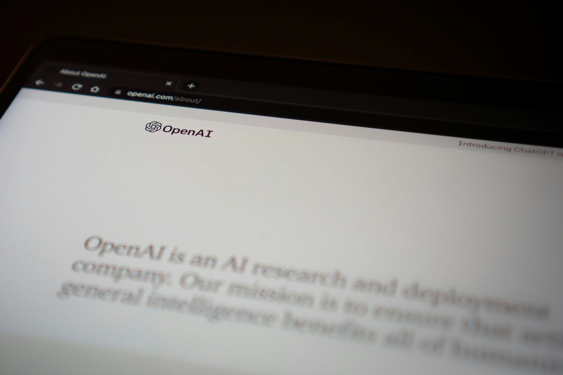 OpenAI homepage displayed on a laptop, featuring the OpenAI logo and mission statement with a minimalist white background