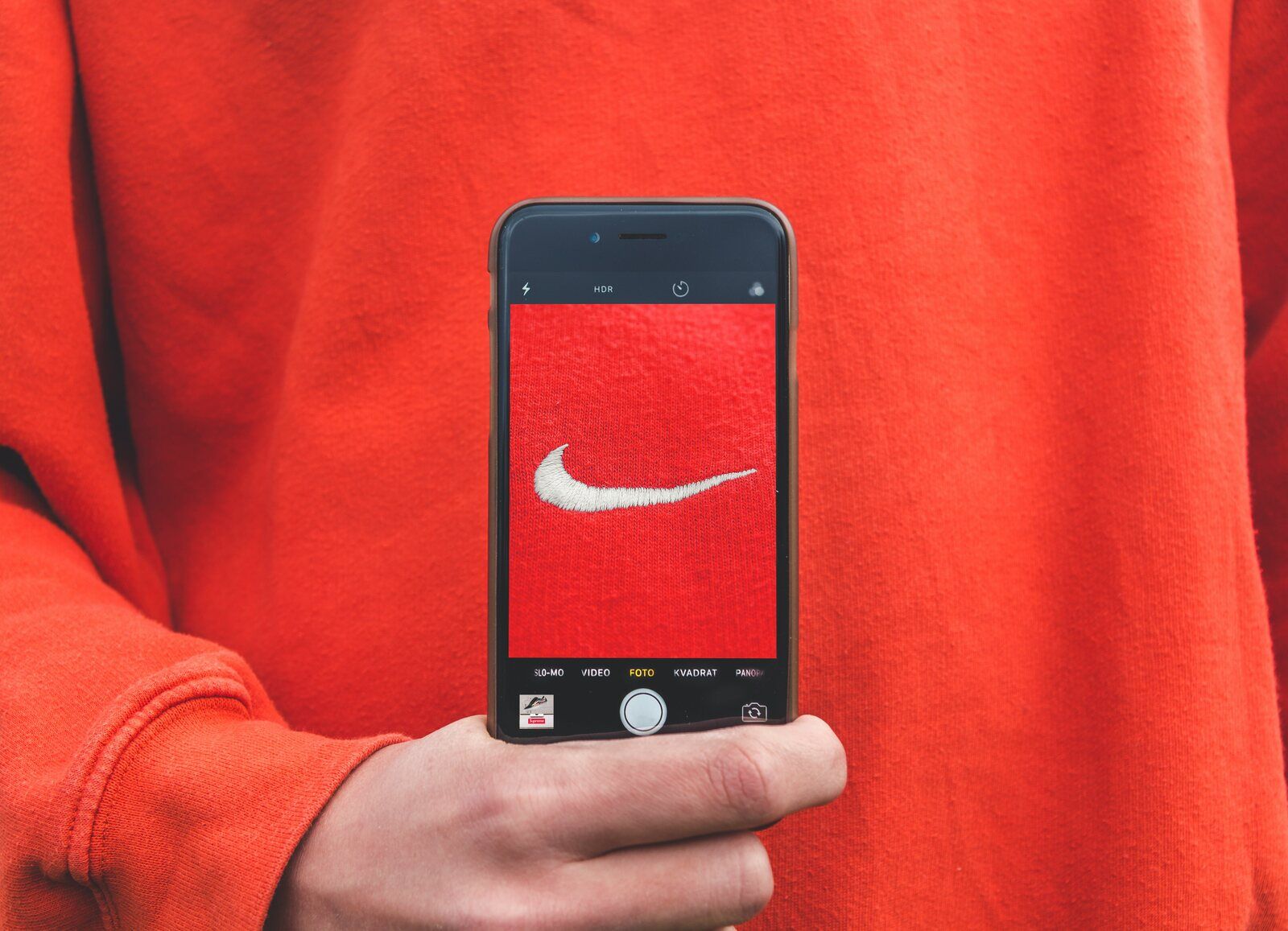 Person holding a phone capturing the iconic Nike swoosh logo embroidered on a red sweatshirt