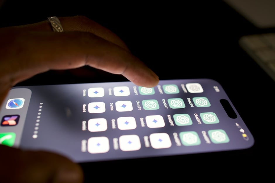 Person using a smartphone with multiple ChatGPT and Gemini app icons displayed on the screen in a dark setting