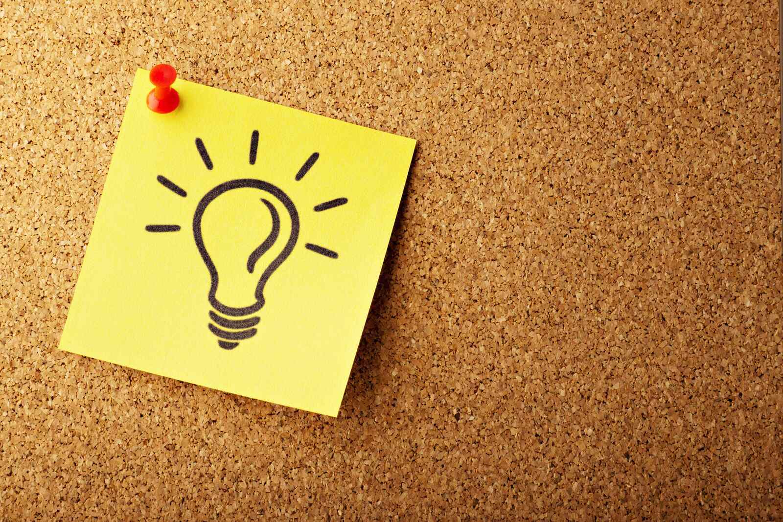 Yellow sticky note with a lightbulb illustration pinned to a corkboard, symbolizing a creative idea